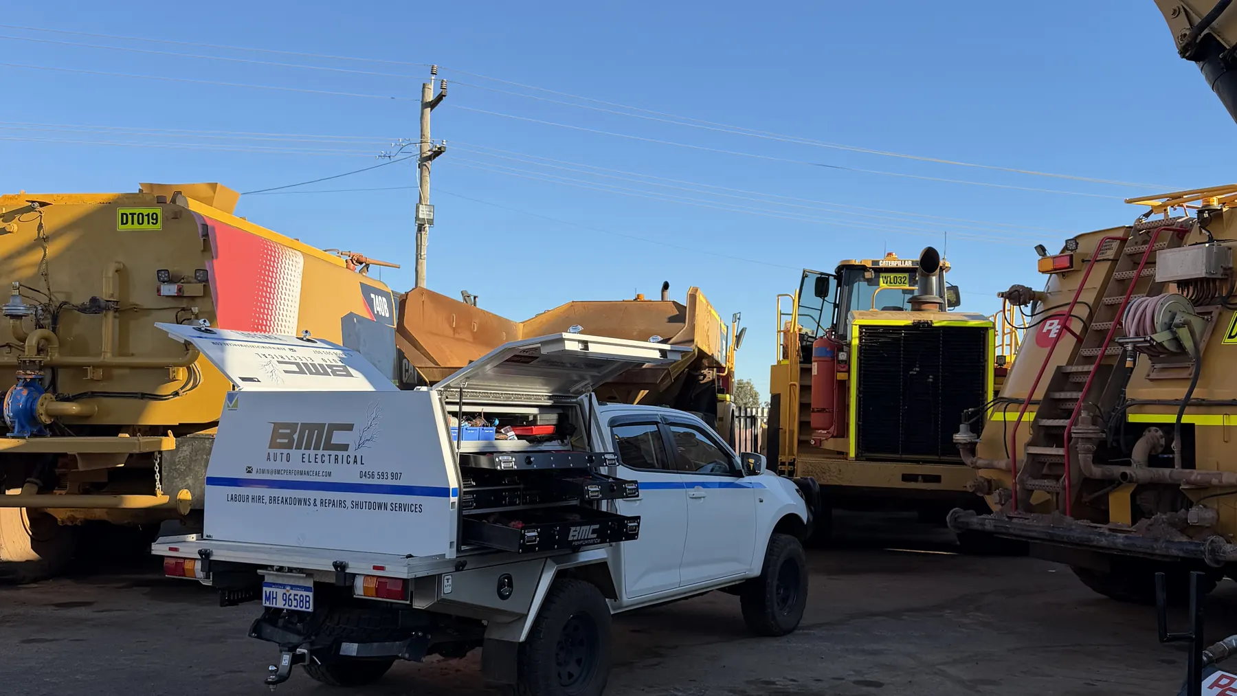 BMC service ute parked among haul trucks and an excavator in a plant yard